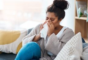A sick woman sneezes into a Kleenex tissue